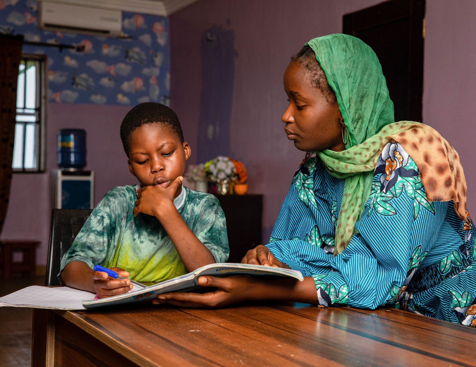 A woman helping a young boy with his schoolwork at a table