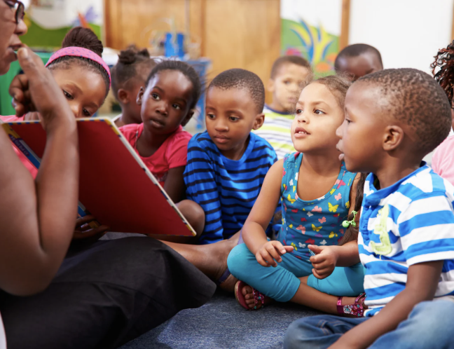 Children gathered around a teacher reading a storybook together.