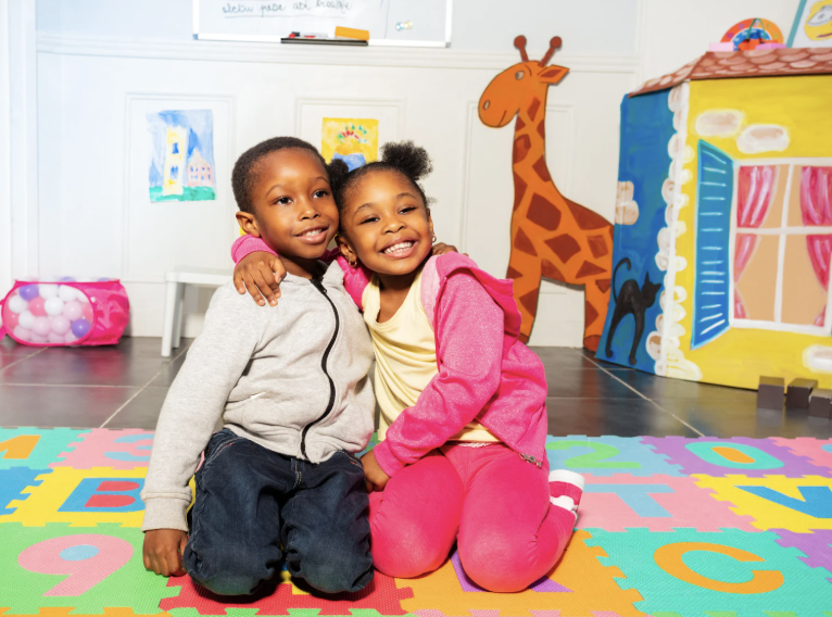 Two children sitting together in a bright, decorated classroom.
